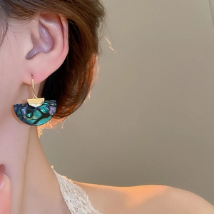 Close-up of fan-shaped abalone shell earrings with gold hooks on a female model