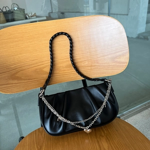 Detail of black pleated cloud bag with braided strap and metal heart chain on wooden chair