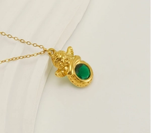 Detailopname van de 18k vergulde engel hanger met groene zirkoon op witte geplooide stof