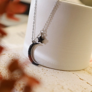 Detailed close-up of crescent moon and star pendant necklace on white ceramic stand