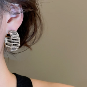 Close-up of a silver C-shaped mesh texture hoop earring worn by a model in a high-fashion shot