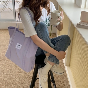 Detail of a purple canvas tote bag with a white minimalist square patch and shoulder straps
