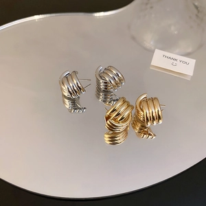Close-up of gold and silver twisted C-shaped earrings on a reflective mirror surface