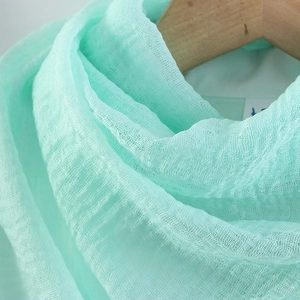 Detailed texture of light green crinkled cotton linen scarf on wooden hanger