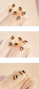 Detailed view of gold and silver oval stud earrings held by white gloved fingers