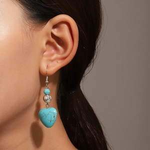 Close-up of heart turquoise drop earring with silver rose bead worn on person