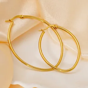 Polished 18k gold oval hoop earrings displayed on soft pink silk with decorative shells