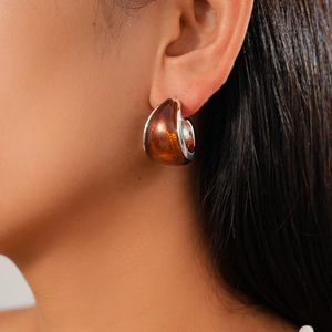 Close-up of amber resin C-shape drop earring with silver metal trim on a female model