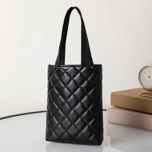 Detailed close-up of a black quilted tote bag on a glass surface with vintage background