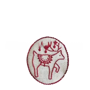 Detailed close-up of handmade embroidered reindeer patch on light linen fabric with red edge
