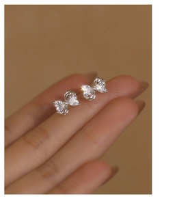 Macro shot of silver bow earrings with sparkling zircons held to show relative size