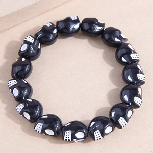 Close-up of black beaded bracelet featuring white skull patterns on textured background