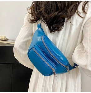 Close-up of blue PU leather waist bag with multiple zippers worn over a white dress