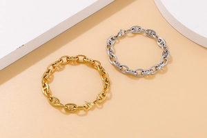 Close-up of gold and silver stainless steel oval link chain bracelets on geometric background