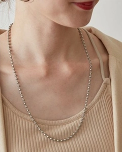 Close-up of silver beaded long necklace worn by model on a beige background