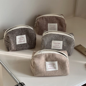 Herringbone wool makeup bags in brown, grey, and pink tones with white zipper