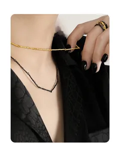 Detailed close-up of textured gold branch necklace and black V-pendant on dark suit