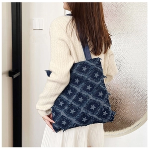Detail of dark blue denim tote bag with star patterns and frayed tassel edges on model