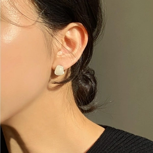 Close-up of a minimalist white translucent pebble stud earring on a model's ear