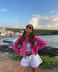 Dettaglio di una giacca fucsia con revers abbinata a crop top e pantaloncini bianchi a vita alta