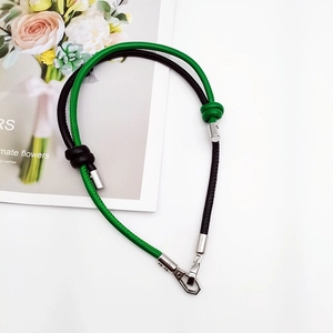 Detail of green and black braided DIY strap with silver metal lobster clasp on white surface