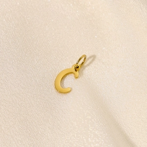 Polierter goldener Edelstahlbuchstabe C Anhänger auf elegantem beige Seidenhintergrund