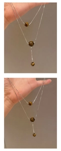 Detail einer silbernen doppellagigen Schlangenkette mit braunen Tigerauge-Perlenanhänger