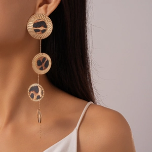 Detailed view of long gold chain earrings with leopard print round pendants on a model