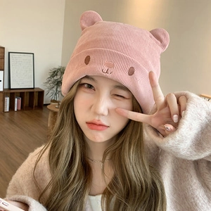 Detail of pink knitted winter hat with cute bear ears and embroidered animal face