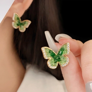 Macro detail of gold-plated butterfly earrings with green stones and sparkling crystals