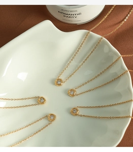 Detailed close-up of gold hexagonal necklaces with zircon pendant on white plate