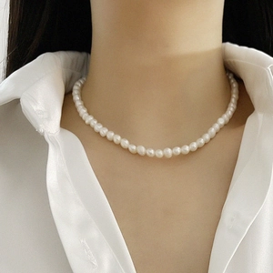 Macro detail of natural freshwater baroque pearl necklace on a white silk shirt