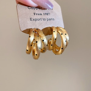 Dettaglio di orecchini a C placcati oro 18k con finitura opaca e pois neri a contrasto