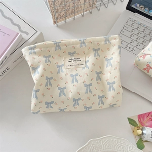 Detalle de neceser de lona crema con lazo azul y estampado floral rosa suave