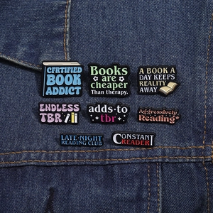 Set of 8 colorful enamel reading pins displayed on a blue denim jacket pocket