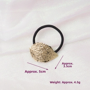 Detail of golden metal leaf hair tie with dimensions 5cm by 3.5cm on white fabric