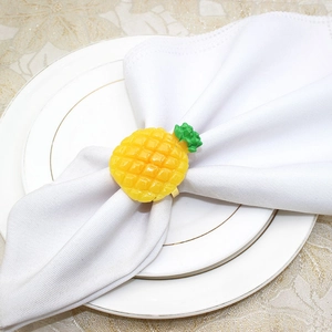 Macro view of a vibrant pineapple napkin ring on a white napkin over dinner plates