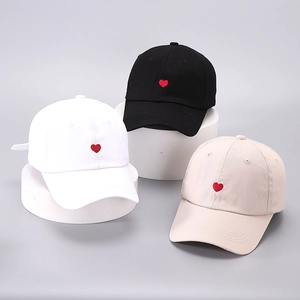 Three cotton baseball caps in black, white, and beige featuring red heart embroidery