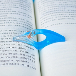 Close-up of a blue resin thumb page holder with gold foil flakes on an open book