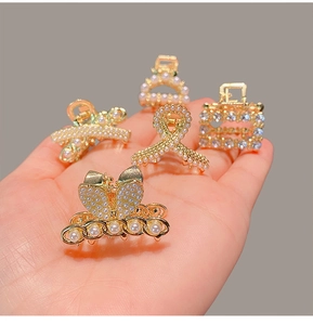 Close-up of five mini gold butterfly and bow hair claws with pearls held in a hand