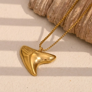 Macro shot of 18K gold plated stingray shark tooth pendant on a sandy texture