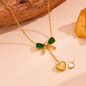 Dettaglio della collana fiocco dorata con gemme verdi a goccia e ciondoli a cuore