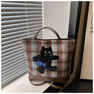 Detail of plaid tote bag featuring a black cat plush patch and brown handle straps