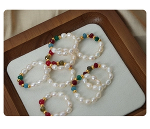 Macro shot of handmade natural pearl beaded rings with colorful gemstone accents on wood tray