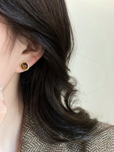 Gros plan de boucles d'oreilles dorées avec œil de tigre sur l'oreille du mannequin