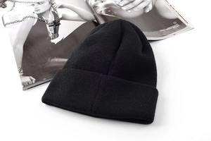 Flat lay of a black ribbed knit beanie with street style magazine and cross necklace