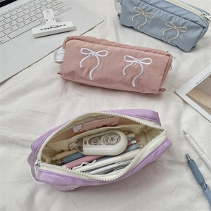 Macro view of high-capacity fabric pencil case interior with embroidered bow and stationery