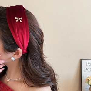Detailed side view of a red velvet headband with a golden bow charm on a model