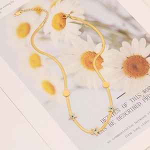 Collier chaîne serpent dorée avec pendentifs étoiles et détails œil bleu sur un magazine