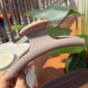 Detail of a large 15cm French matte pink hair claw clip held in bright natural sunlight